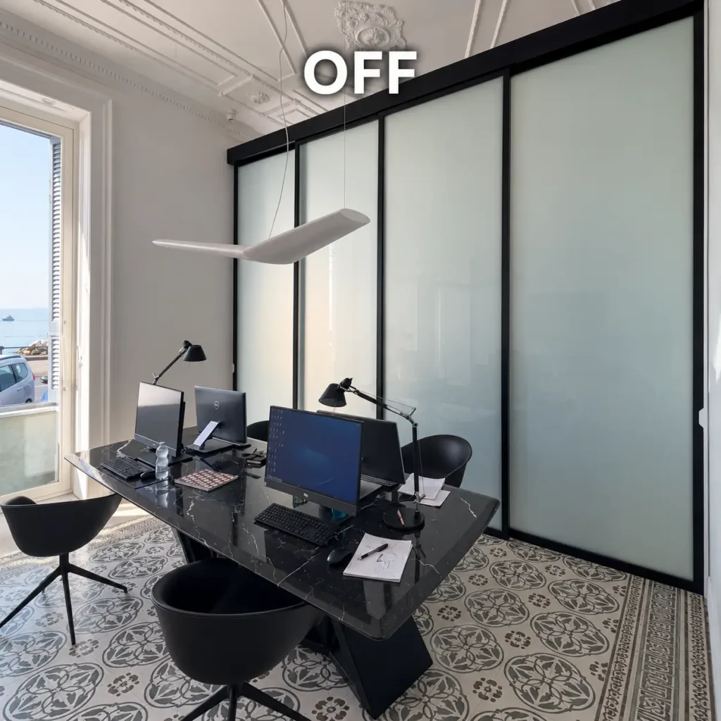 Ufficio moderno con parete divisoria in vetro intelligente trasparente, struttura nera e sala riunioni visibile, soluzione per privacy su richiesta, luminosità e separazione elegante degli spazi professionali.